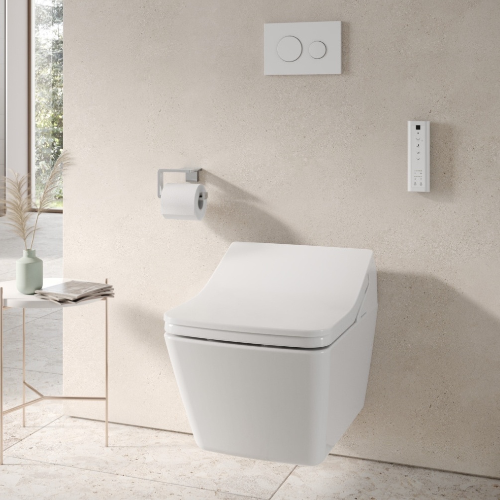 Lifestyle image of the TOTO Washlet SX Auto Flush Rimless Wall Hung Toilet mounted on a beige tiled bathroom wall, aside a bathroom caddy